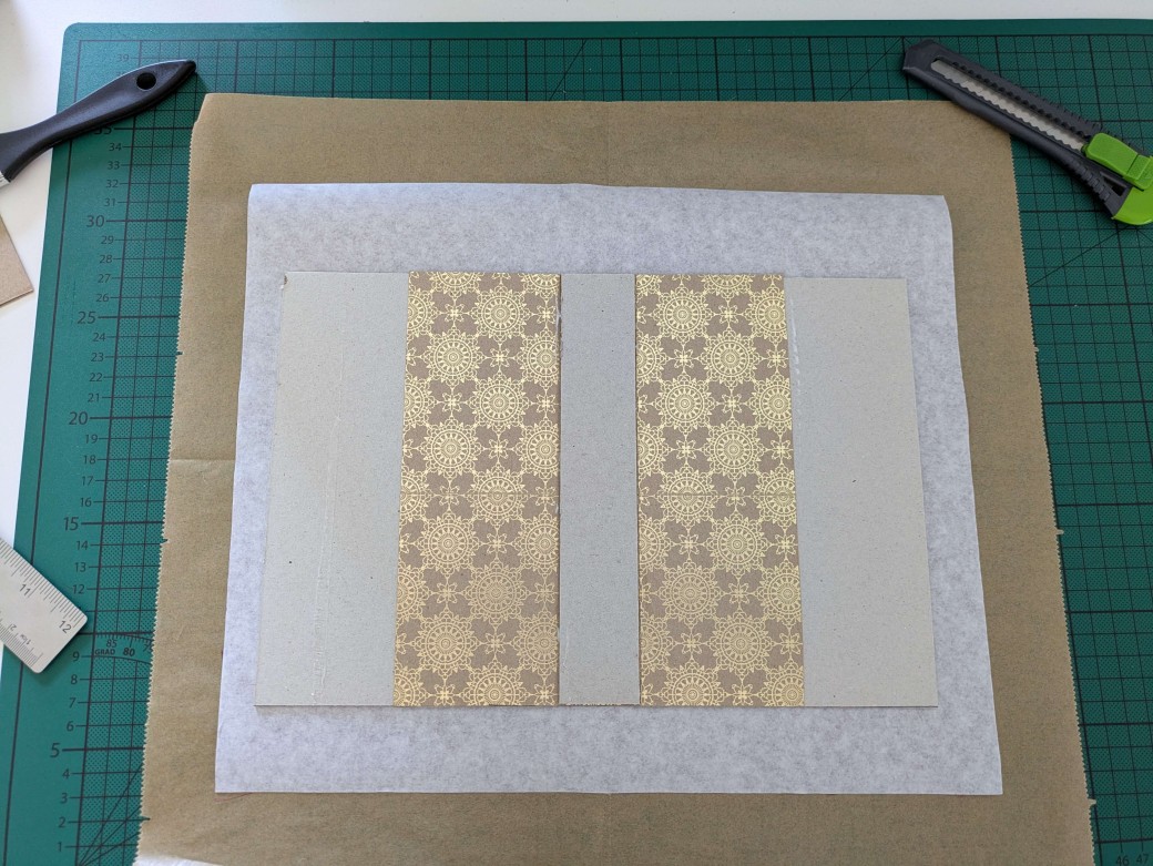 The hardcover casing is shown lying on top of the book cloth inside, with a sheet of baking paper underneath it to prevent glue to spill in the workspace.